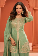 Load image into Gallery viewer, Woman wearing a green embroidered traditional outfit with a pink background