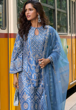Load image into Gallery viewer, Woman in a blue embroidered outfit standing in front of a yellow train.
