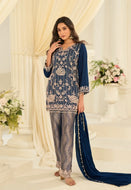 Woman in a blue and silver embroidered outfit with a flowing scarf in a decorated indoor setting.