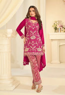 Woman wearing a pink traditional outfit with intricate patterns in a decorated room.