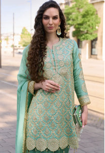 Woman in a light green embroidered traditional outfit standing outdoors.