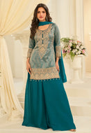 Woman wearing a teal and gold traditional outfit in a decorated room.